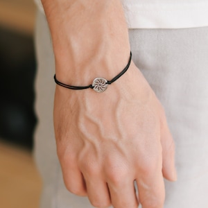 Può includere: Un braccialetto in corda nera con un ciondolo d'argento a forma di sole.