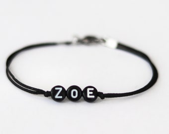 May include: A black string bracelet with the name "ZOE" spelled out in white letters on black beads.