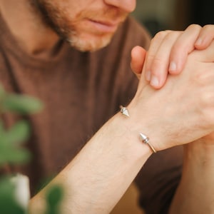 Może przedstawiać: Srebrna bransoletka z dwoma ostrymi końcami. Bransoletka jest noszona na nadgarstku osoby o brązowej skórze.