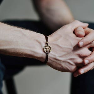 Peut inclure: Un bracelet en cuir marron avec un charme en or en forme de symbole Om.