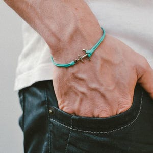 May include: A turquoise blue cord bracelet with a silver anchor charm.