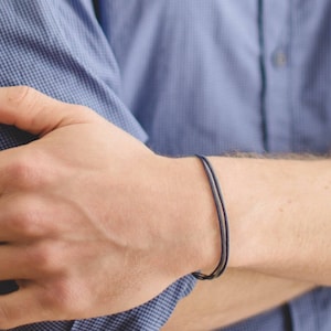 May include: A simple bracelet with two thin cords, one navy blue and one gray, worn on a person's wrist.