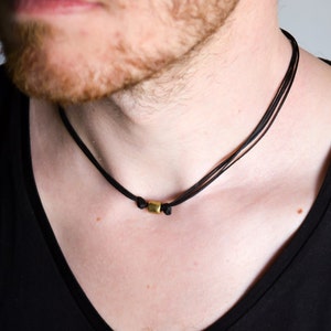 May include: A simple black cord necklace with a small gold square pendant.