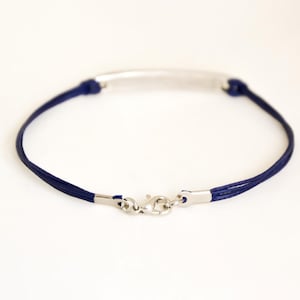 Pu&ograve; includere: Un braccialetto in corda blu navy con una barra e una chiusura argentate.