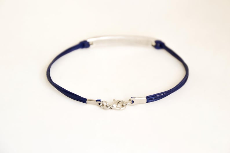 Pu&ograve; includere: Un braccialetto in corda blu navy con una barra e una chiusura argentate.