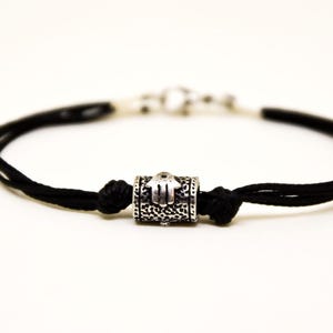 May include: A black cord bracelet with a silver charm featuring a hamsa hand design.