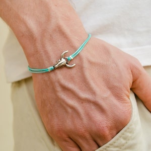 Könnte beinhalten: Ein türkisfarbenes Armband aus Kordel mit einem silbernen Stierkopf-Anhänger.
