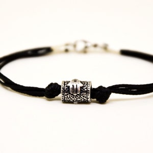 May include: A black cord bracelet with a silver charm featuring a hamsa hand design.
