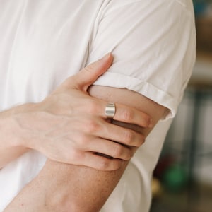 Puede incluir: Un anillo de plata con forma rectangular plana. El anillo se lleva en el dedo índice de una mano.