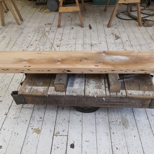Pu&ograve; includere: Un lungo ripiano in legno rustico realizzato con legno riciclato, con nodi e imperfezioni, che poggia su un carrello di metallo con ruote. Il ripiano &egrave; di colore marrone chiaro e ha una finitura naturale e invecchiata.