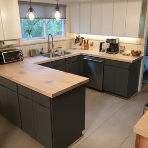 K&ouml;nnte beinhalten: Eine moderne K&uuml;che mit grauen Schr&auml;nken, hellen Holz-Arbeitsplatten und Edelstahlger&auml;ten. Die K&uuml;che hat eine U-f&ouml;rmige Anordnung mit einem Fenster &uuml;ber der Sp&uuml;le und Pendelleuchten.