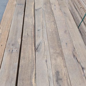 K&ouml;nnte beinhalten: Ein Stapel verwitterter, hellbrauner Holzbretter. Die Bretter haben ein nat&uuml;rliches, rustikales Aussehen mit sichtbarer Maserung und &Auml;sten. Das Holz scheint wiederverwertet oder gealtert zu sein, mit einer leicht rauen Textur.