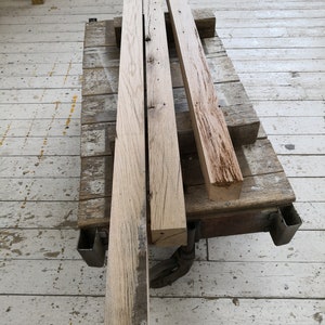 Puede incluir: Tres piezas de tablones de madera toscamente labrados y desgastados en un carro de madera. Los tablones son de color marr&oacute;n claro con nudos y patrones de veta de color marr&oacute;n oscuro.