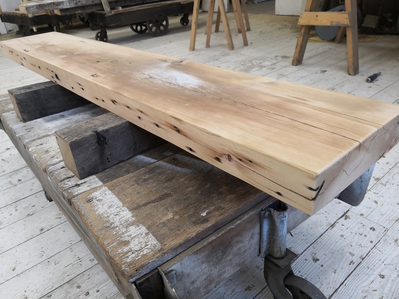 Pu&ograve; includere: Un lungo ripiano in legno marrone chiaro con una finitura grezza e naturale. Il ripiano &egrave; sostenuto da due travi in legno e ha un aspetto rustico e recuperato.
