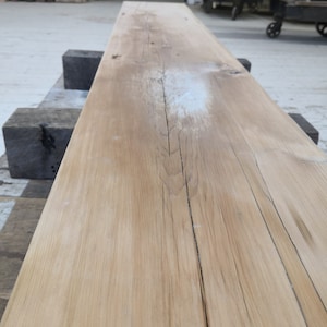 Pu&ograve; includere: Primo piano di una tavola di legno marrone chiaro con alcuni nodi e un segno bianco. La tavola &egrave; liscia e ha una venatura del legno naturale.