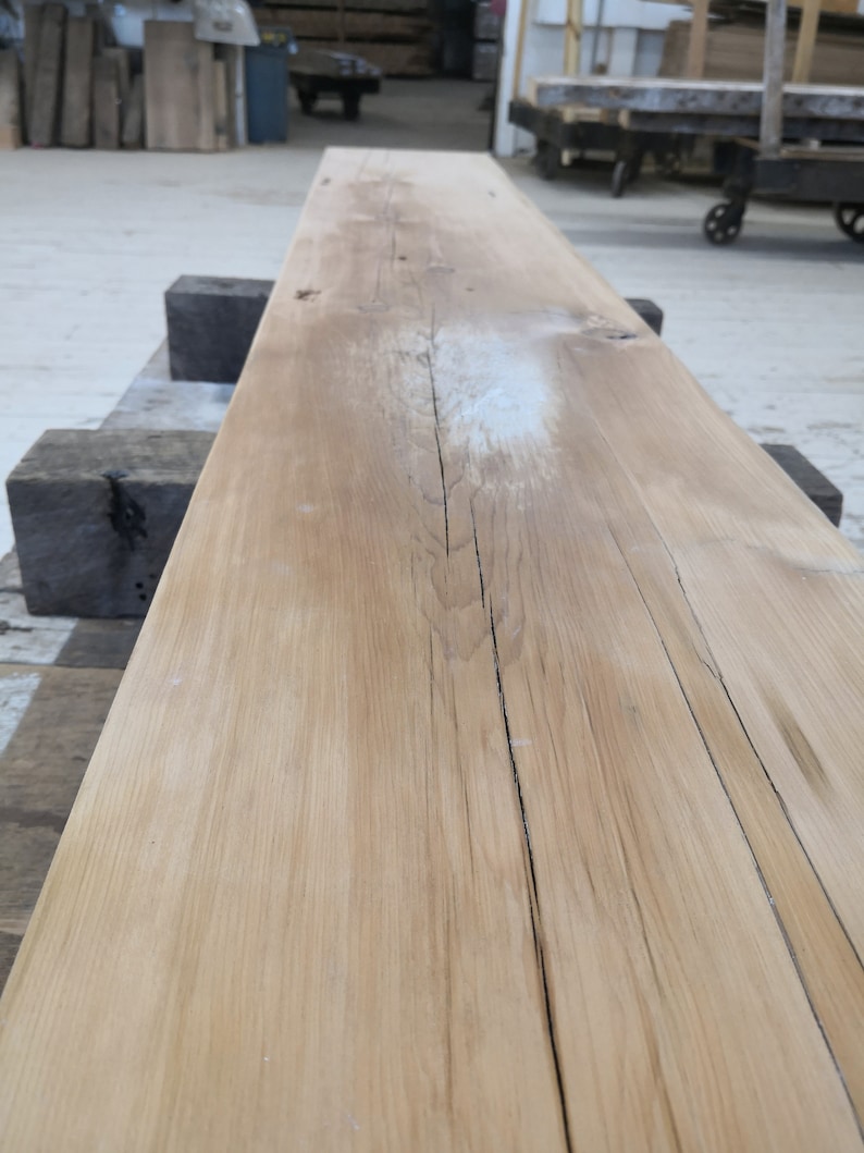Pu&ograve; includere: Primo piano di una tavola di legno marrone chiaro con alcuni nodi e un segno bianco. La tavola &egrave; liscia e ha una venatura del legno naturale.