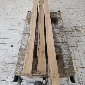 Puede incluir: Cuatro piezas de tablones de madera sin terminar, apiladas unas sobre otras, en una plataforma de madera con ruedas.