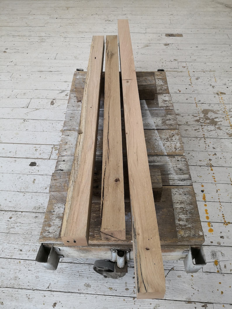 Puede incluir: Cuatro piezas de tablones de madera sin terminar, apiladas unas sobre otras, en una plataforma de madera con ruedas.