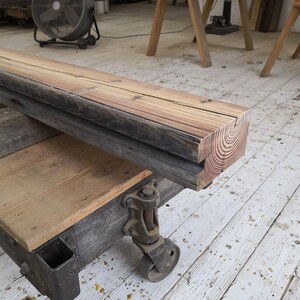 K&ouml;nnte beinhalten: Ein rustikaler Holzbalken mit sichtbarer Maserung und Jahresringen. Er liegt auf einer Holzplattform mit Metallr&auml;dern, was eine wiederverwendete industrielle &Auml;sthetik suggeriert. Das Holz hat ein verwittertes, gealtertes Aussehen.