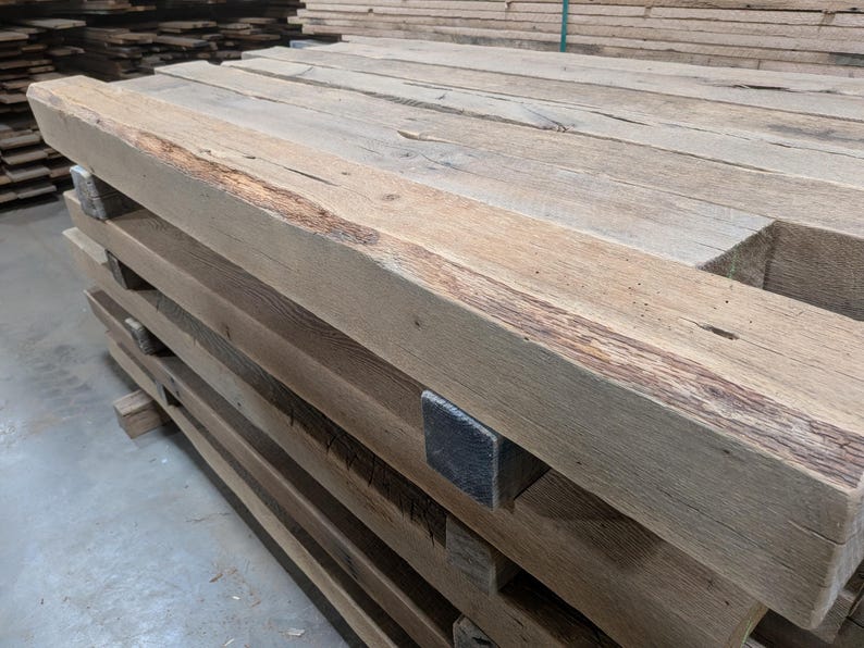 K&ouml;nnte beinhalten: Ein Stapel verwitterter, rechteckiger Holzbalken. Die Balken sind hellbraun mit sichtbarer Holzmaserung und Knoten. Einige Balken weisen dunklere braune Streifen und eine raue, strukturierte Oberfl&auml;che auf. Die Enden der Balken sind rechtwinklig geschnitten.
