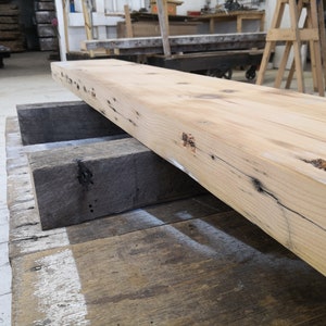 Pu&ograve; includere: Un'ampia tavola di legno di colore chiaro con nodi e motivi di venatura. La tavola &egrave; appoggiata su due tavole di legno pi&ugrave; piccole.