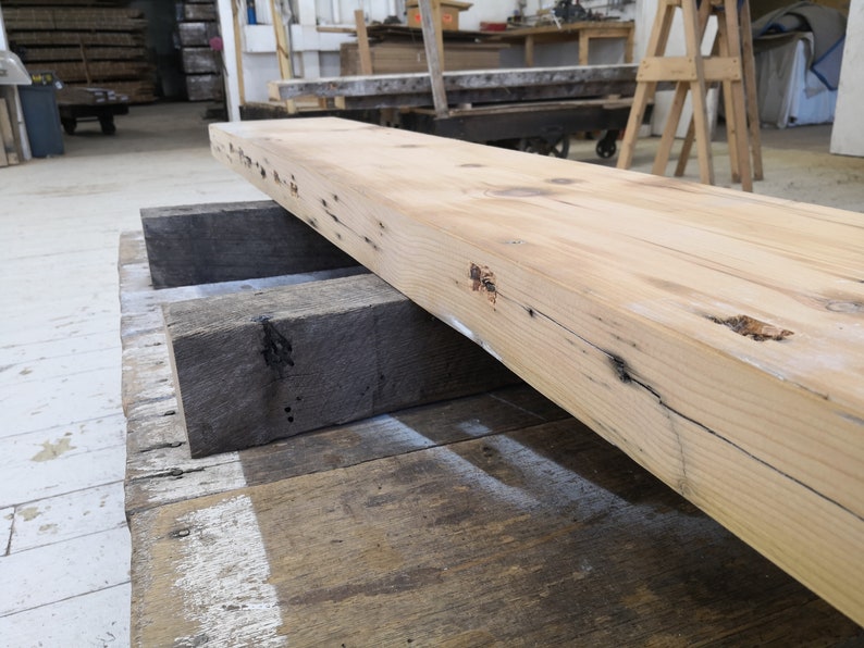 Pu&ograve; includere: Un'ampia tavola di legno di colore chiaro con nodi e motivi di venatura. La tavola &egrave; appoggiata su due tavole di legno pi&ugrave; piccole.