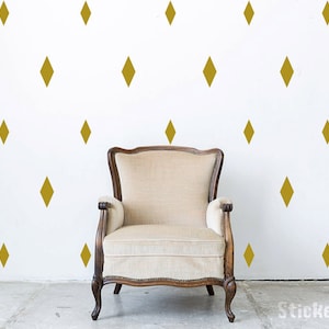 May include: A white armchair with wooden arms and legs sits in front of a white wall with a repeating pattern of gold diamond shapes.