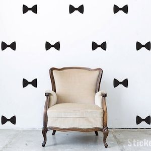 May include: A white wall with black bow tie decals, a brown armchair sits in front of the wall.