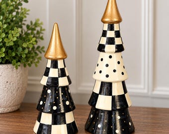 May include: Two decorative tree-shaped ornaments featuring a gold-painted conical top. The surfaces are decorated with alternating black and white checkered patterns and black sections with white polka dots, creating a distinct geometric design.