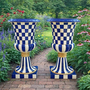 May include: Two large, decorative urns with a blue and white checkered pattern. The urns have a blue rim, a white and blue striped base, and a gold-colored accent. They are placed on a brick pathway surrounded by a garden.