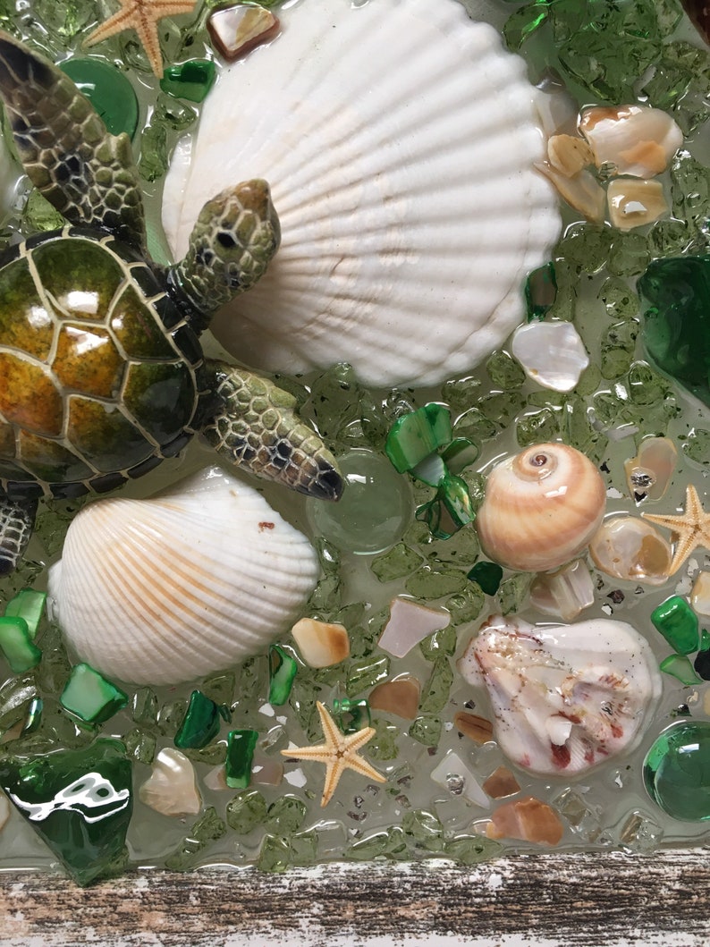 Puede incluir: Una figurita de tortuga verde con una concha blanca, rodeada de piezas de vidrio verde y marr&oacute;n, conchas blancas y una estrella de mar.