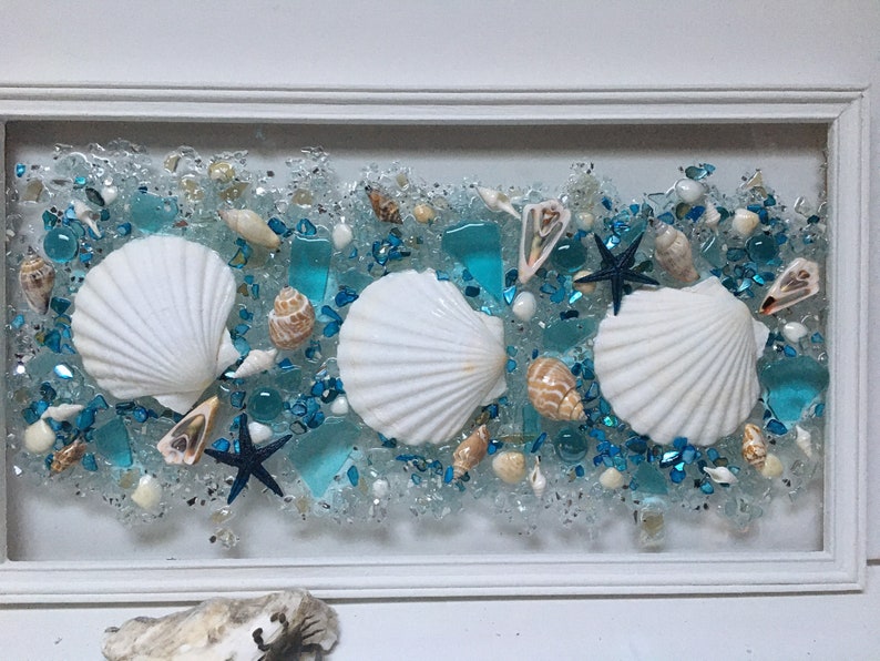 May include: A framed seashell art piece with three white seashells, blue glass pieces, and a starfish on a white background.