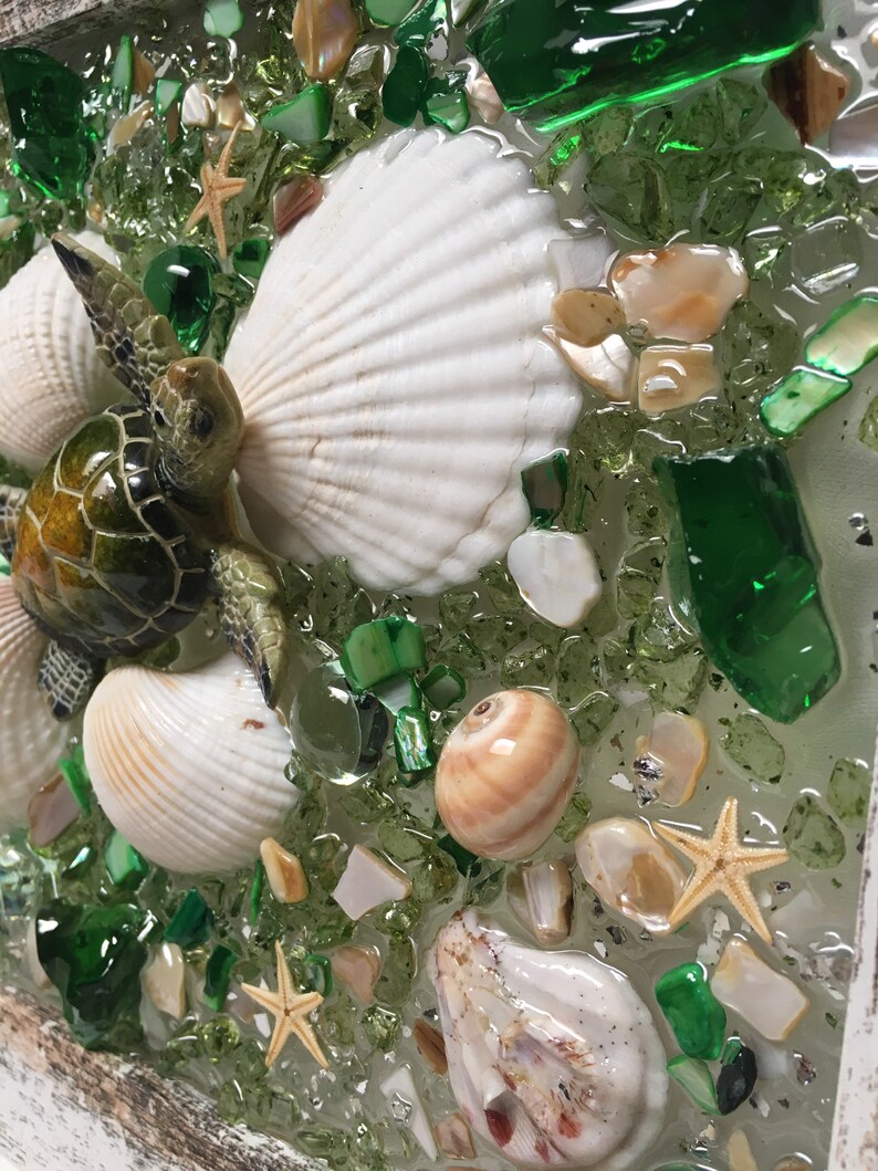 Puede incluir: Una pieza de arte de resina con una tortuga marina, conchas marinas y estrellas de mar en un lecho de piezas de vidrio verde y blanco.