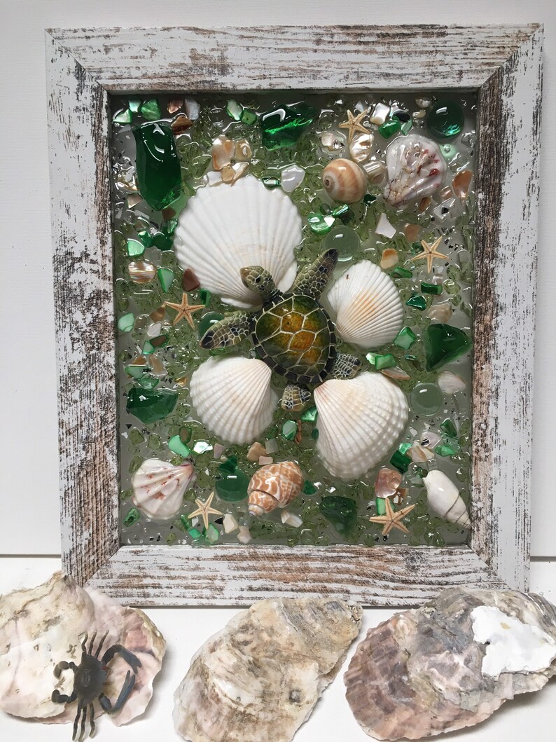 Puede incluir: Una pieza de arte de resina enmarcada con un mosaico de conchas marinas y vidrio de mar verde, blanco y marr&oacute;n. Una peque&ntilde;a figura de tortuga verde se encuentra en el centro del mosaico.