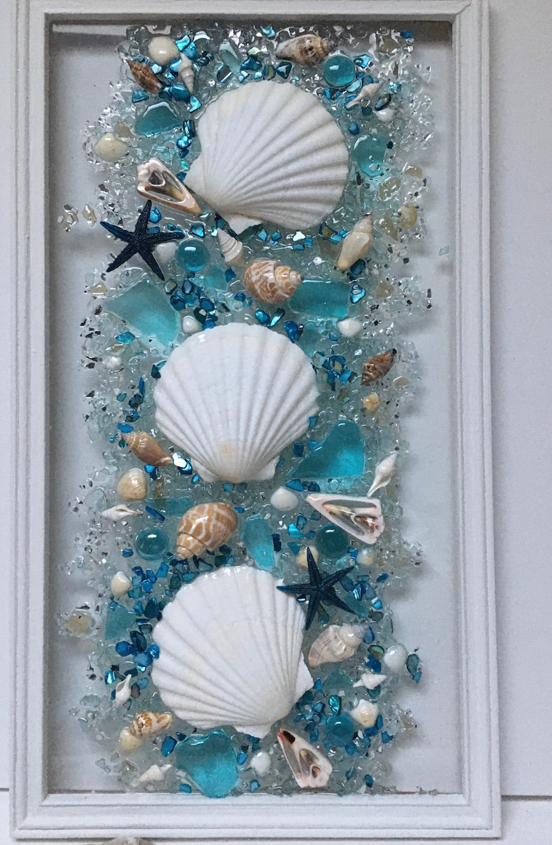 May include: A framed artwork featuring three white seashells, blue and white glass pieces, and starfish on a white background.