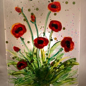 Peut inclure: Une veilleuse avec un motif en verre color&eacute; de coquelicots rouges avec des tiges et des feuilles vertes sur un fond blanc. La veilleuse est branch&eacute;e sur une prise de courant.