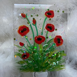 Peut inclure: Une veilleuse en verre avec un motif de fleurs de coquelicot rouges. Les fleurs sont peintes sur un panneau de verre transparent avec des tiges et des feuilles vertes. La veilleuse a une base blanche &agrave; brancher.