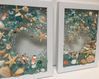 May include: Two white framed square wall art pieces with a blue, green, and white seashell and starfish design.
