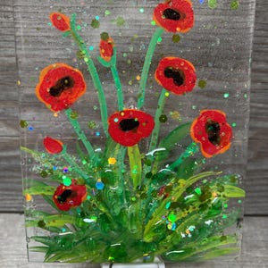 Peut inclure: Un veilleuse en verre teint&eacute; repr&eacute;sentant un motif de coquelicot rouge avec des feuilles vertes et des accents de paillettes dor&eacute;es.