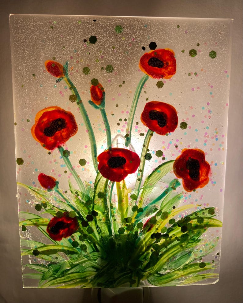 Peut inclure: Un veilleuse en verre teint&eacute; repr&eacute;sentant des coquelicots rouges avec des tiges et des feuilles vertes sur un fond blanc avec des accents de paillettes.