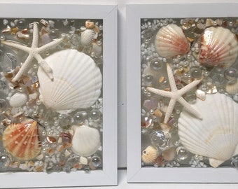 May include: Two white framed pictures with a seashell and starfish theme. Each picture has a variety of seashells, starfish, and glass beads in a clear resin.