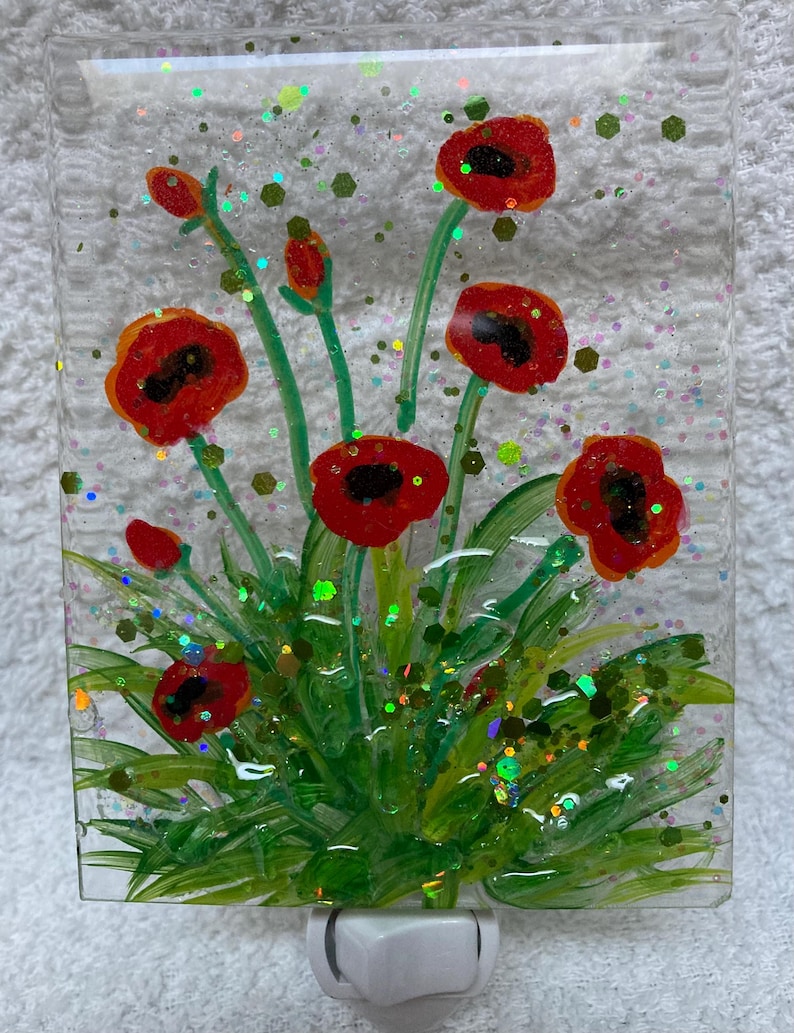 Peut inclure: Une veilleuse en verre avec une image peinte de coquelicots rouges et de feuillage vert. Le verre est d&eacute;cor&eacute; de paillettes iris&eacute;es.