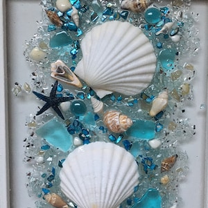May include: A framed seashell art piece with white seashells, blue glass, and a starfish on a white background.