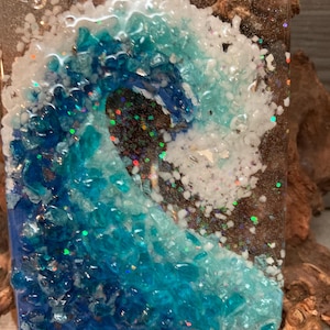 May include: A blue and white glass night light with a wave design. The wave is made of small pieces of glass and glitter. The night light is plugged into an outlet.