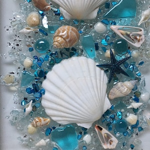 May include: A white seashell with a blue starfish and blue and white sea glass on a white background.