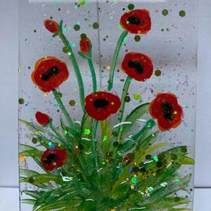 Peut inclure: Une veilleuse en verre avec une image peinte de coquelicots rouges et de feuilles vertes. Le verre est recouvert de paillettes iris&eacute;es.