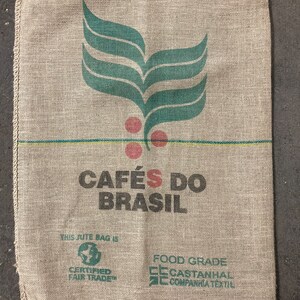 May include: A brown burlap sack with a green leaf design and the text "CAF&Eacute;S DO BRASIL". The sack also has the text "THIS JUTE BAG IS CERTIFIED FAIR TRADE" and "FOOD GRADE CECASTANHAL COMPANHIA TEXTIL".