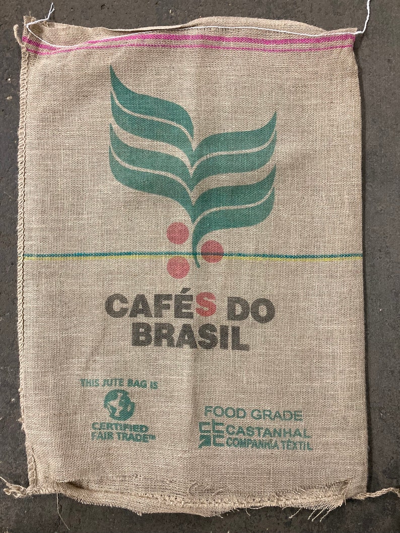 May include: A brown burlap sack with a green leaf design and the text "CAF&Eacute;S DO BRASIL". The sack also has the text "THIS JUTE BAG IS CERTIFIED FAIR TRADE" and "FOOD GRADE CECASTANHAL COMPANHIA TEXTIL".