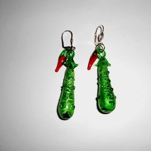 Könnte beinhalten: Ein Paar grüne Glasohrringe in Form von Gurken mit roten Glaschilis, die von oben hängen.