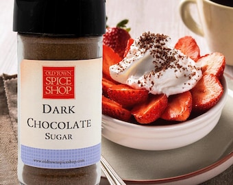 Könnte beinhalten: Ein Glas Dark Chocolate Sugar von Old Town Spice Shop steht neben einer Schüssel mit geschnittenen Erdbeeren, die mit Schlagsahne und Schokoladenraspeln belegt sind. Im Hintergrund eine Tasse Kaffee.